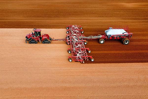 Red tractor pulling 5 wheel seeder against dry red/brown soil during seeding time